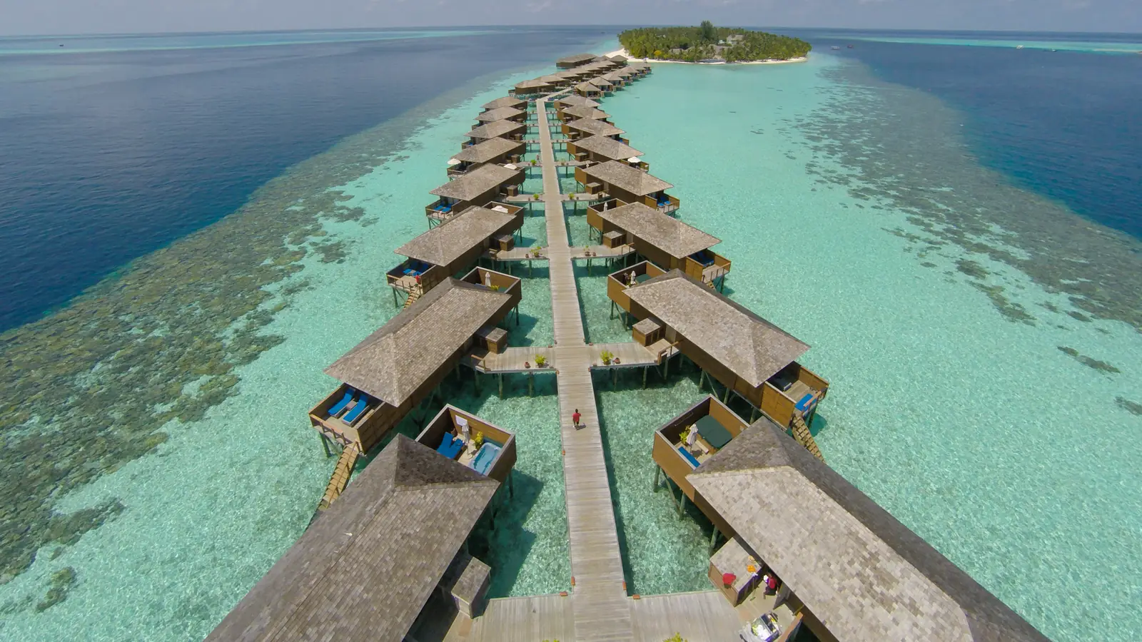 Rows of overwater villas on a long jetty over turquoise lagoon water in the Maldives